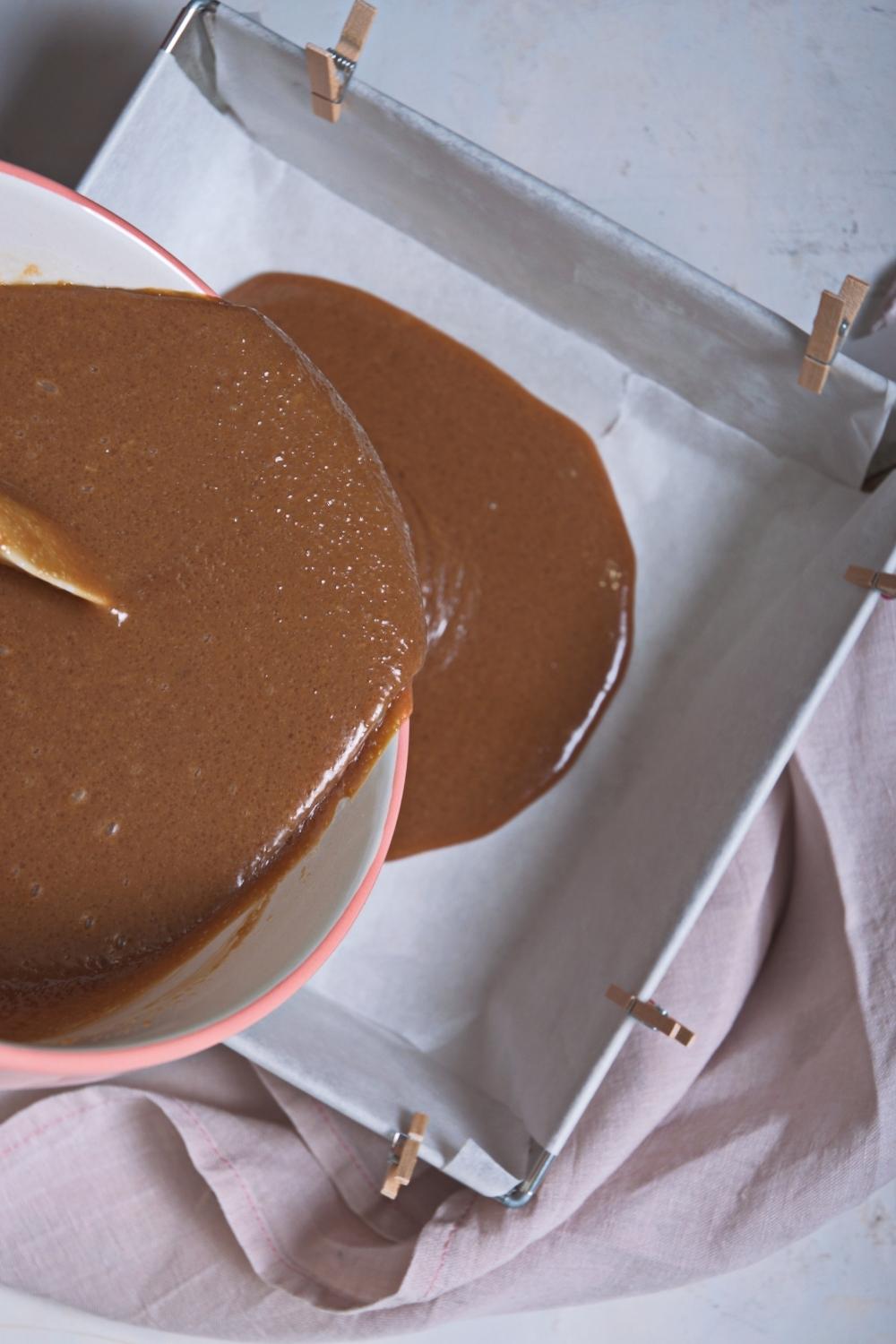 An overhead view of a bowl containing melted caramel fudge ingredients being poured into a parchment paper lined square pan.
