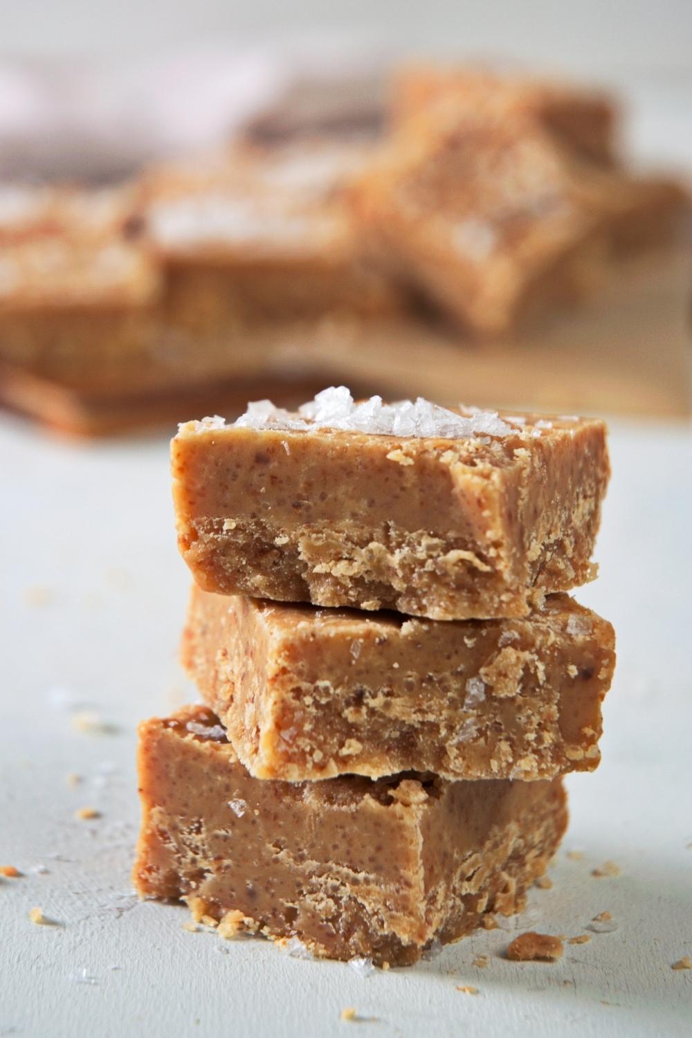 A stack of three caramel fudge squares. Salted caramel is garnished on top.