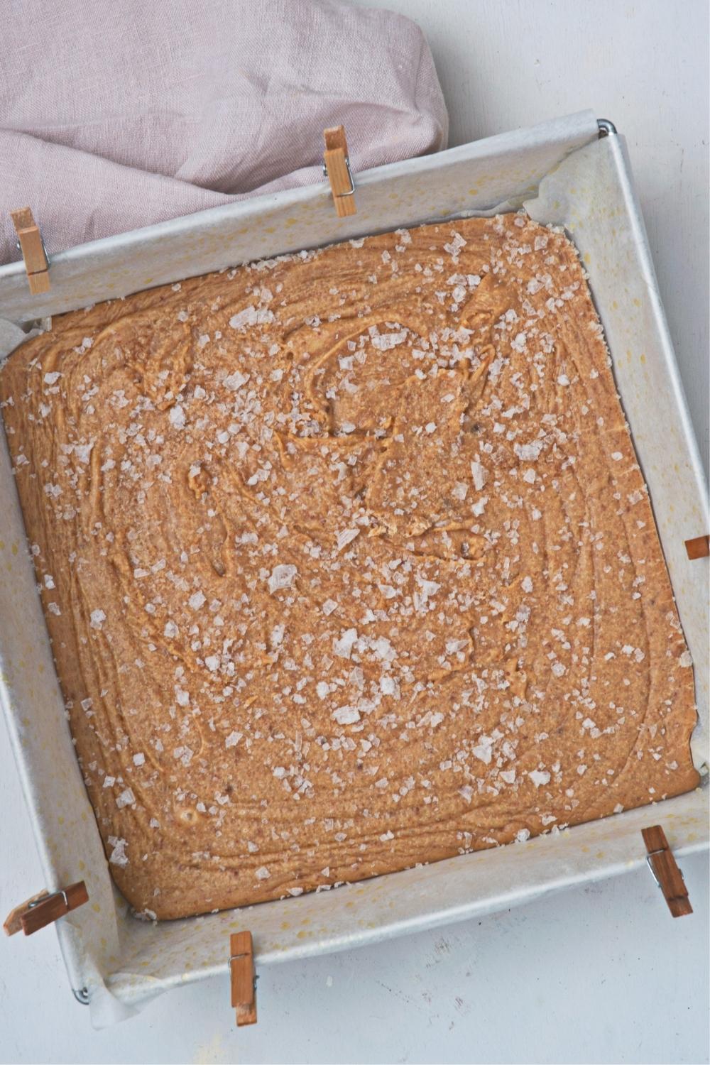 An overhead view of a square pan lined with parchment paper containing caramel fudge that has been set for two hours.