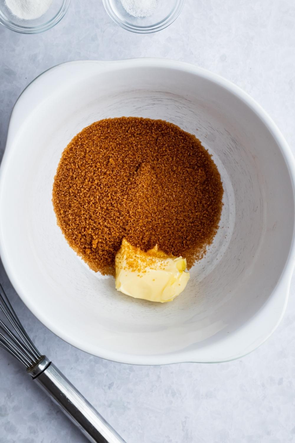 An overhead view of a large mixing bowl containing sugar and butter.