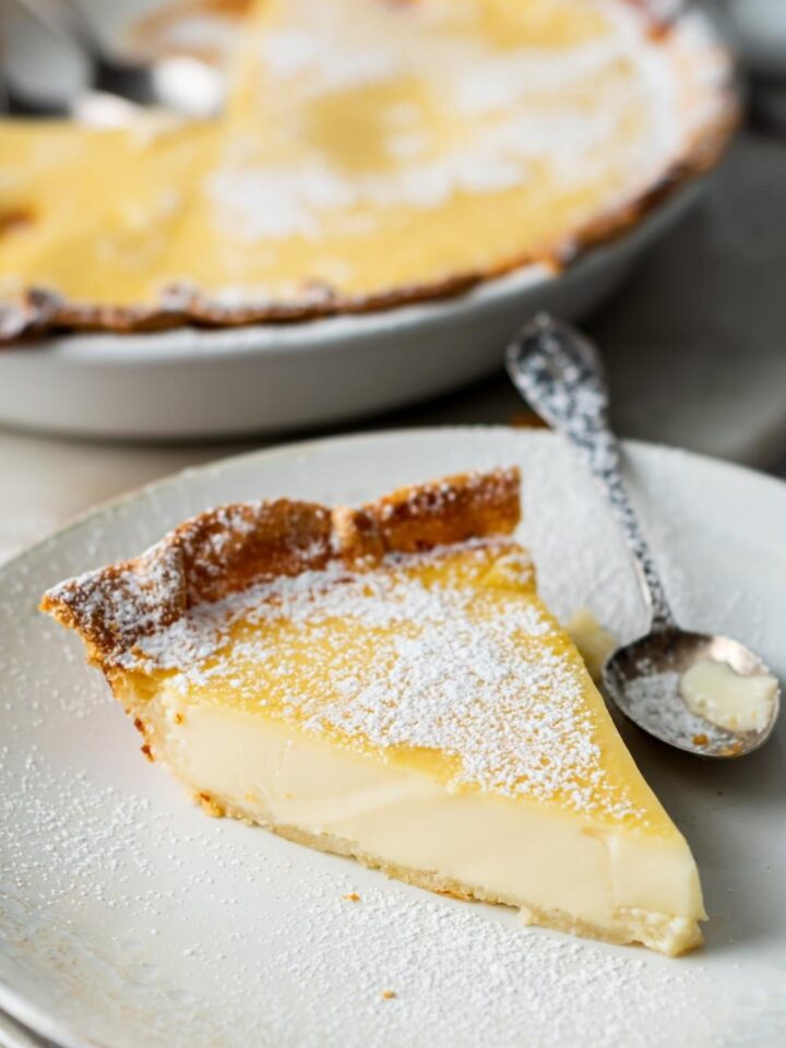 A close up of a slice of custard pie on a serving plate and a spoon sitting next to it.