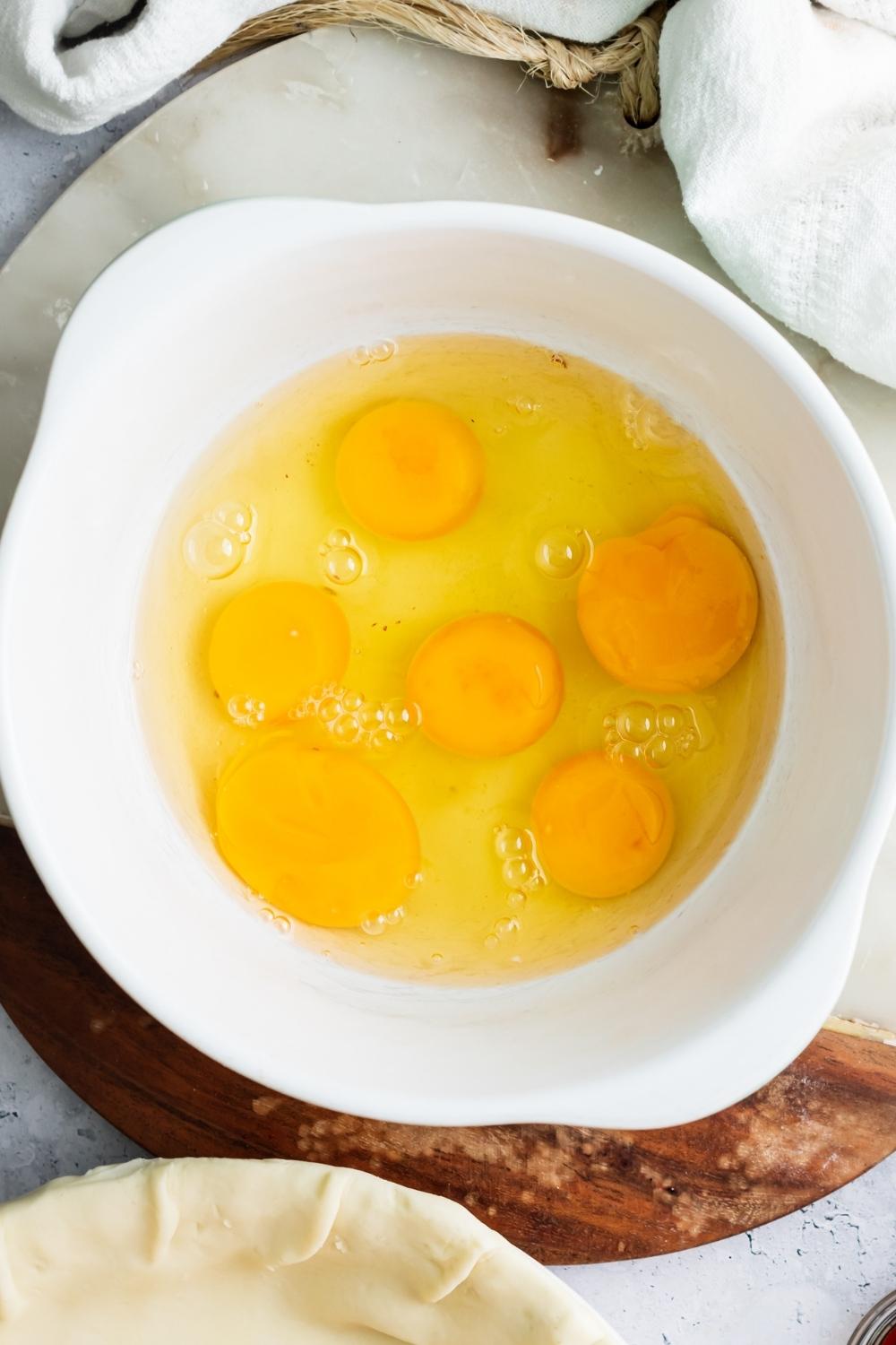 An overhead view of 6 eggs cracked into a large mixing bowl.