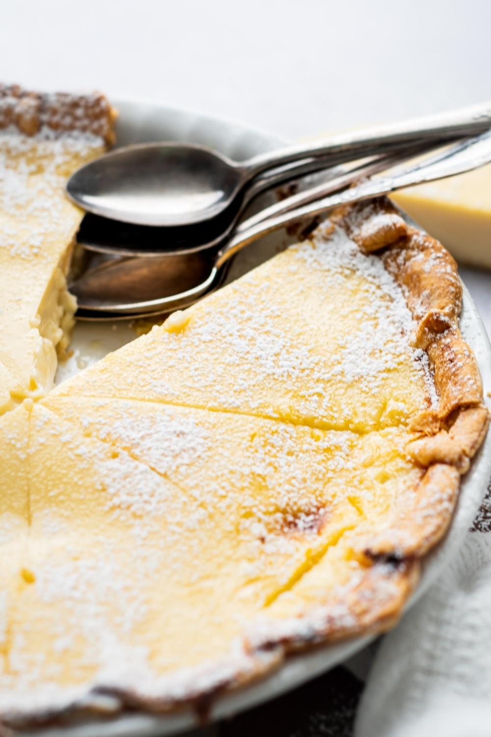 A close up of custard pie sprinkled with powdered sugar with a slice missing. Two spoons sit where the slice was.