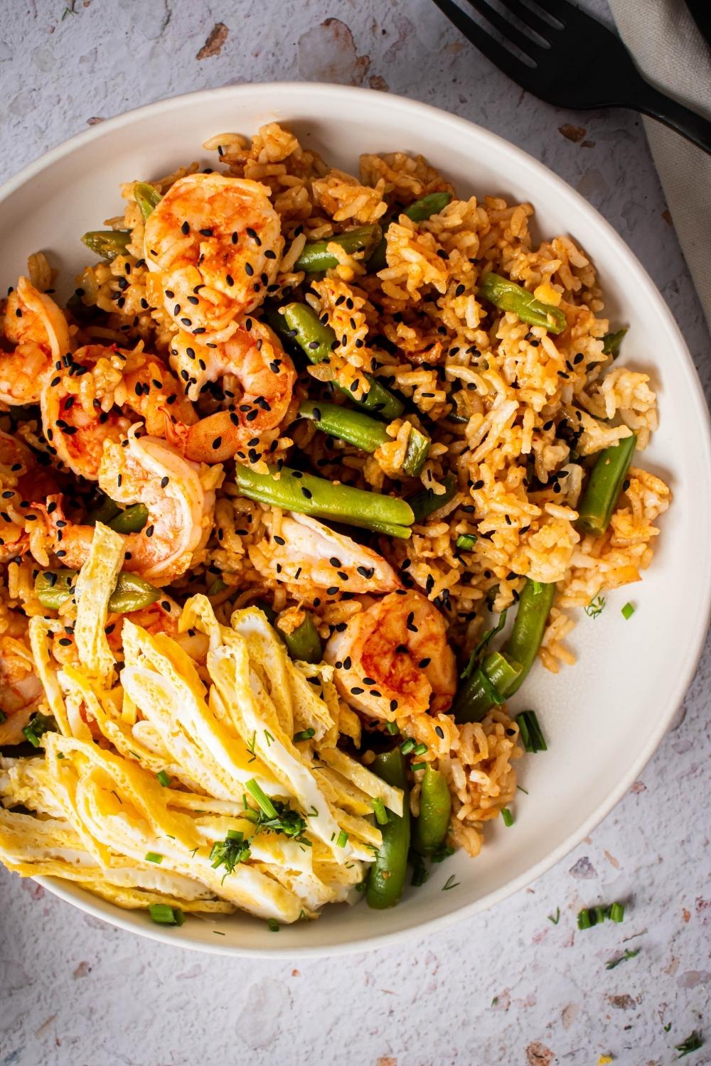 An overhead, close-up view of a bowl of Cajun Fried Rice with green beans, shrimp, and egg.