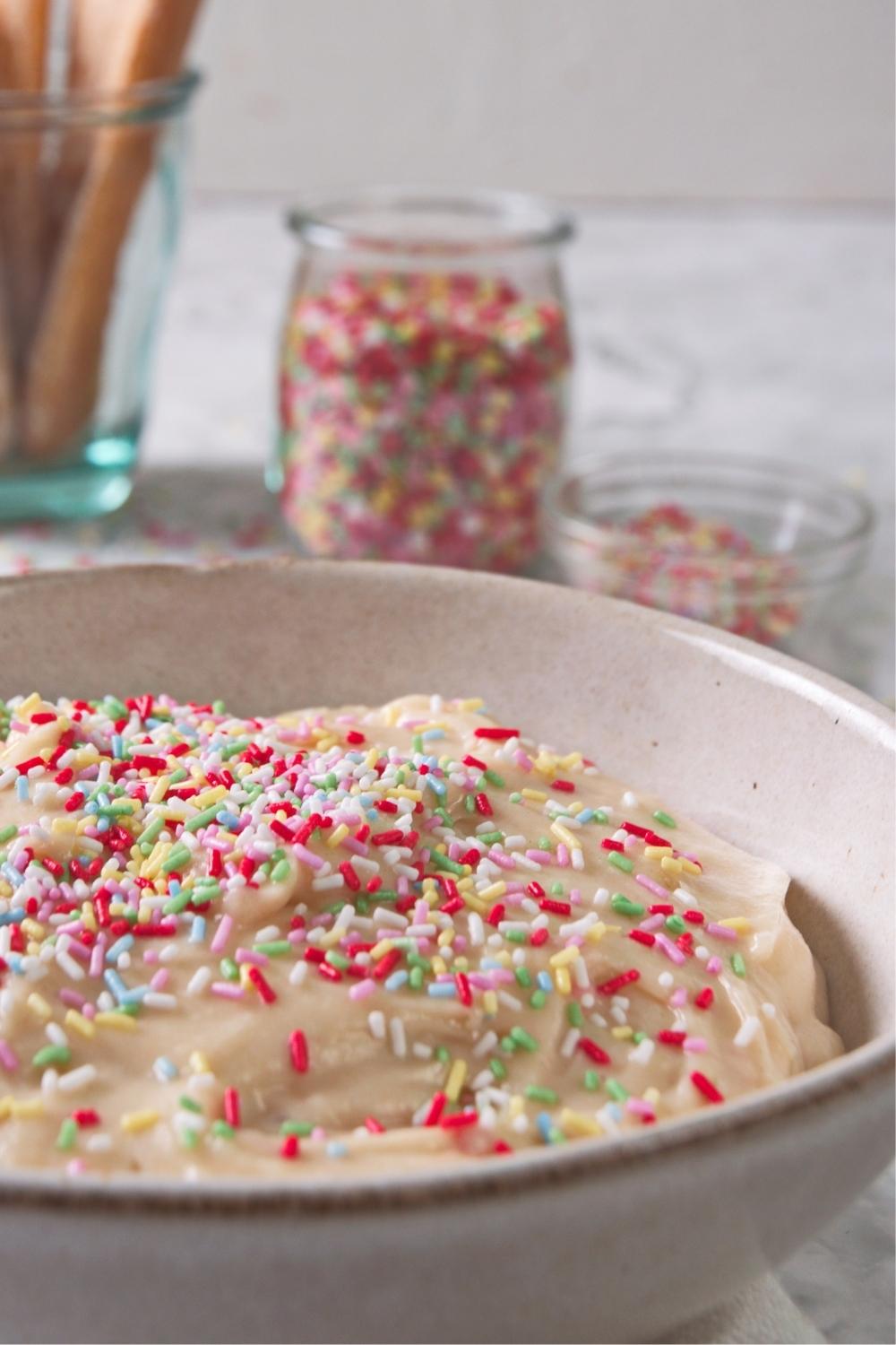 A close-up of a serving bowl containing homemade dunkaroo dip topped with rainbow sprinkles.