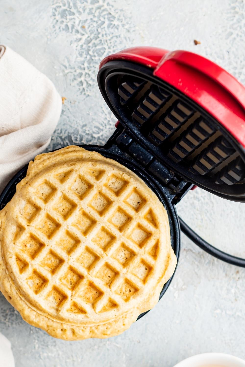 An overhead view of a waffle iron and a cooked waffle on it.