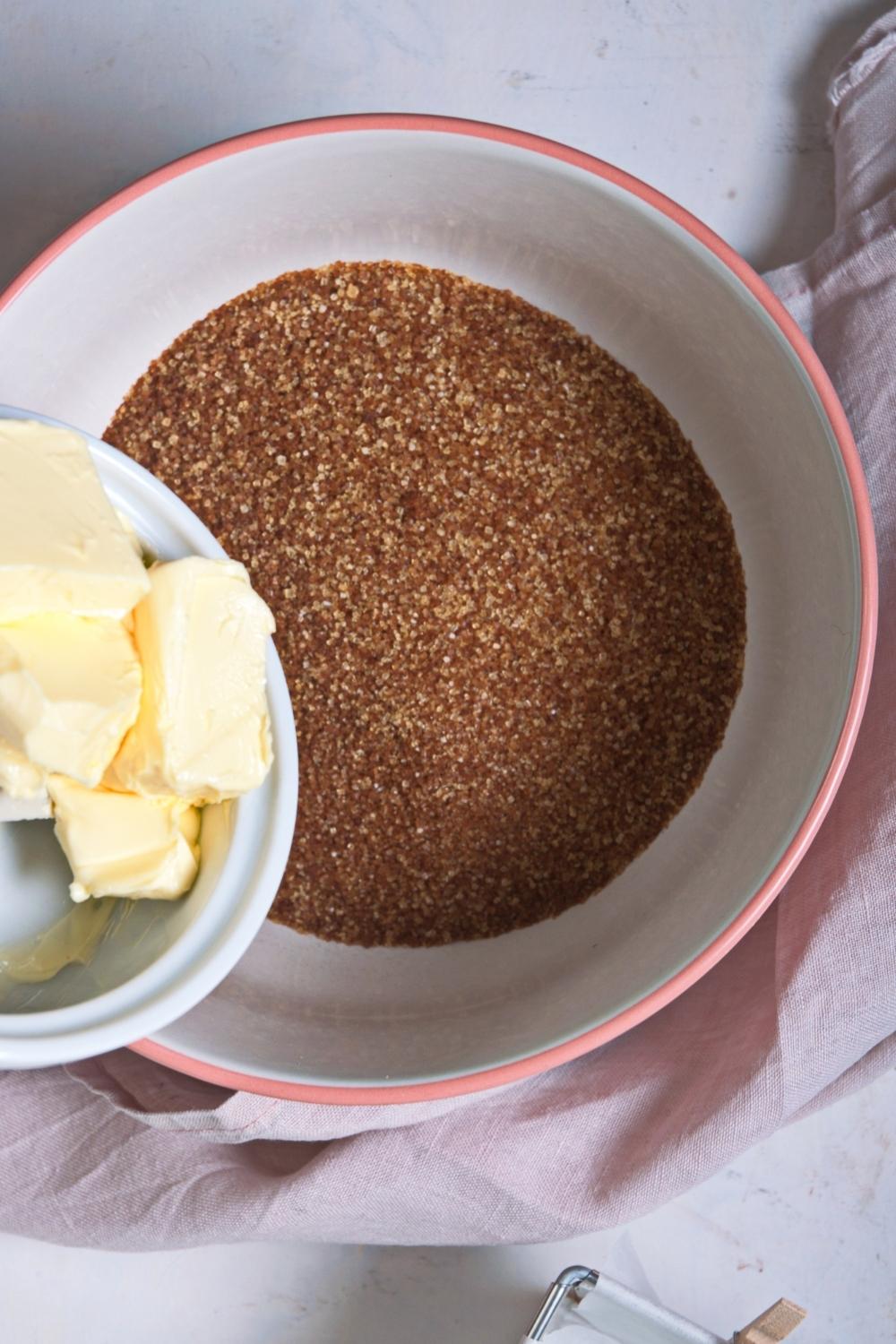 An overhead view of a large bowl containing brown sugar with a smaller bowl containing butter being poured into it.