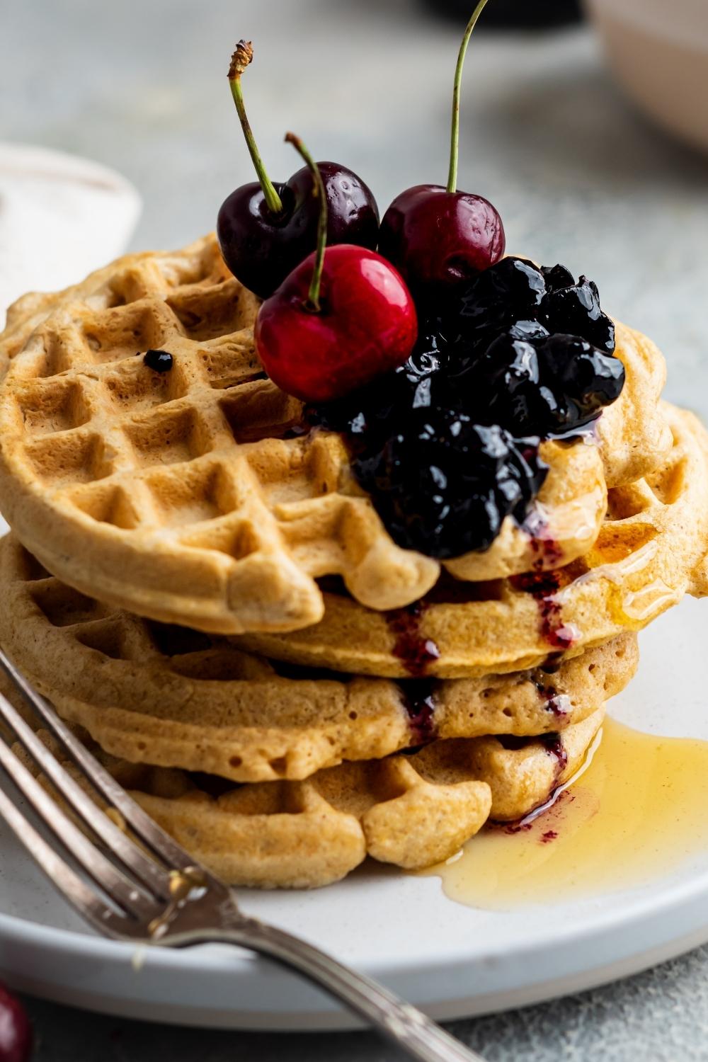 A stack of four homemade waffles without milk, drizzled with honey and topped with fresh berries and cherries.