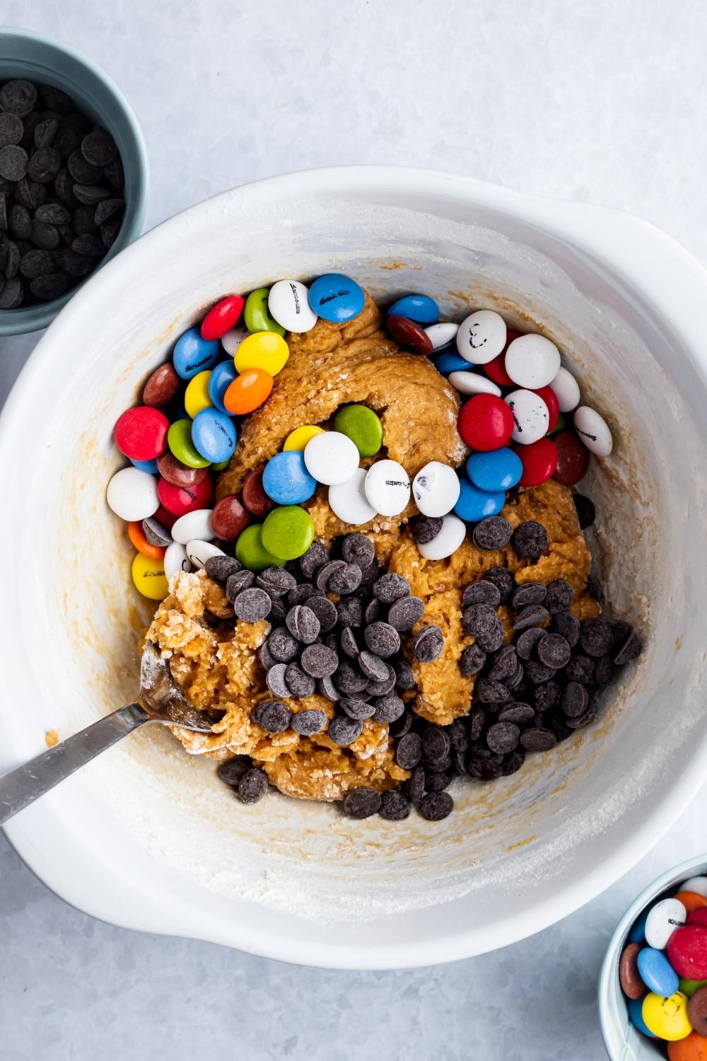 An overhead view of sugar cookie dough in a large mixing bowl; M&Ms and chocolate chips have just been added.