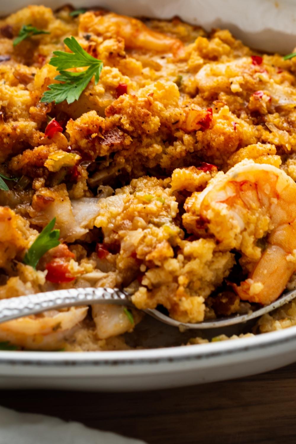 A close-up of a serving dish with cooked homemade seafood stuffing. A spoon has taken a scoop with a shrimp in it.