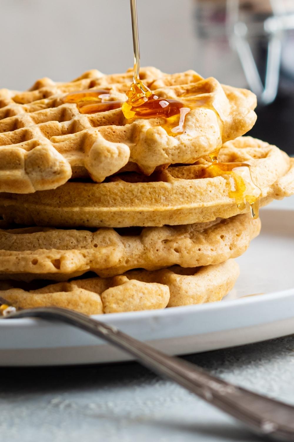 A close up of a stack of four homemade waffles without milk in drizzled with honey.