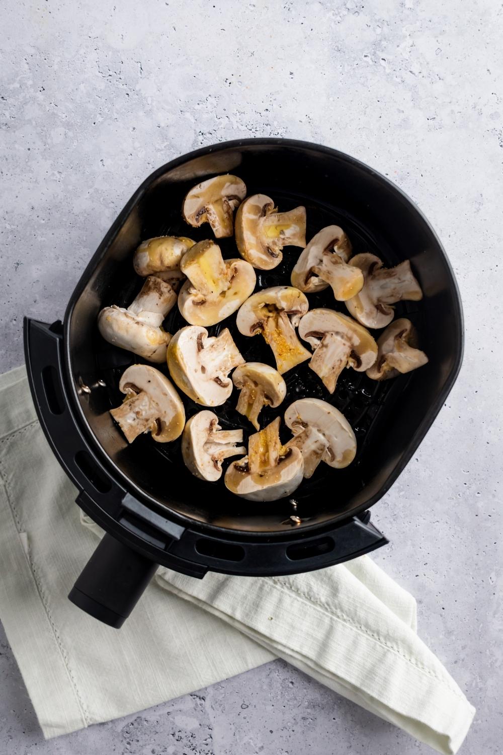 A bunch of mushrooms with olive oil on top in an air fryer basket.