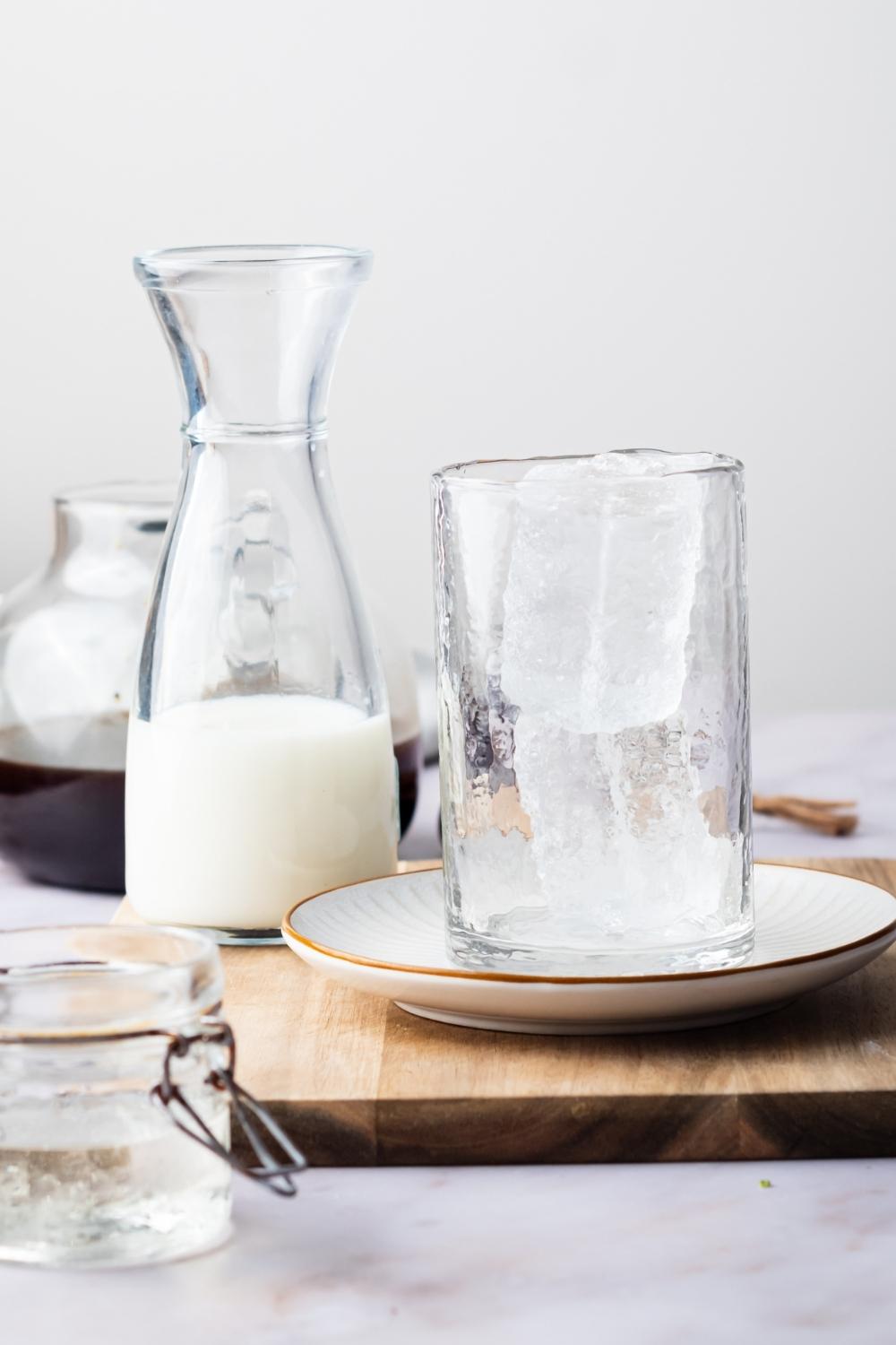 A glass with two big ice cubes, a pitcher with half and half, and coffee picture containing black coffee.