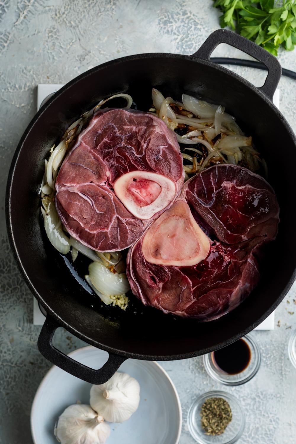 A dutch oven filled with two beef shanks and onions.
