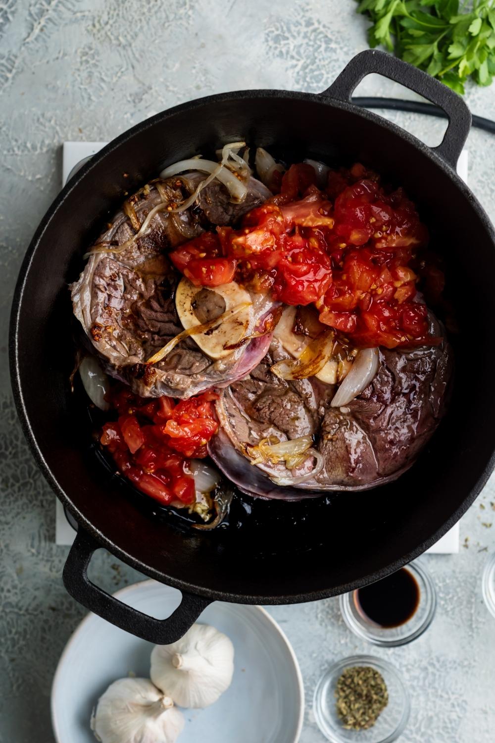 A dutch oven filled with crushed tomatoes, onion, and beef shank,