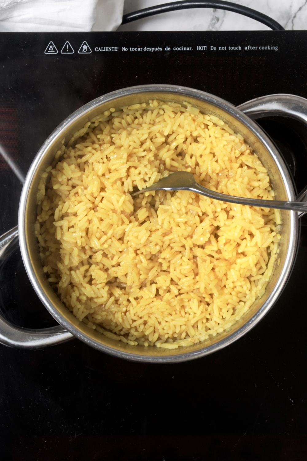 A fork in a pot filled with yellow rice on top of a burner.
