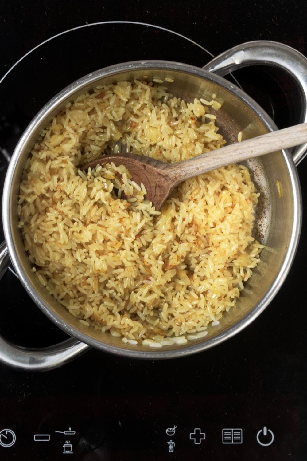 Yellow rice in a pot with a wooden spoon in it.