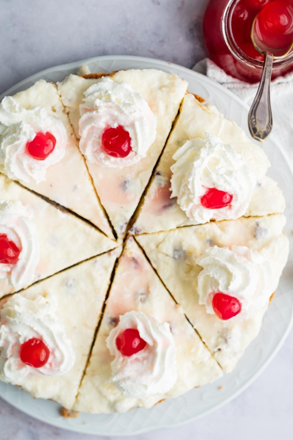 An overhead view of a homemade million dollar pie sliced and topped with whipped cream and cherries.