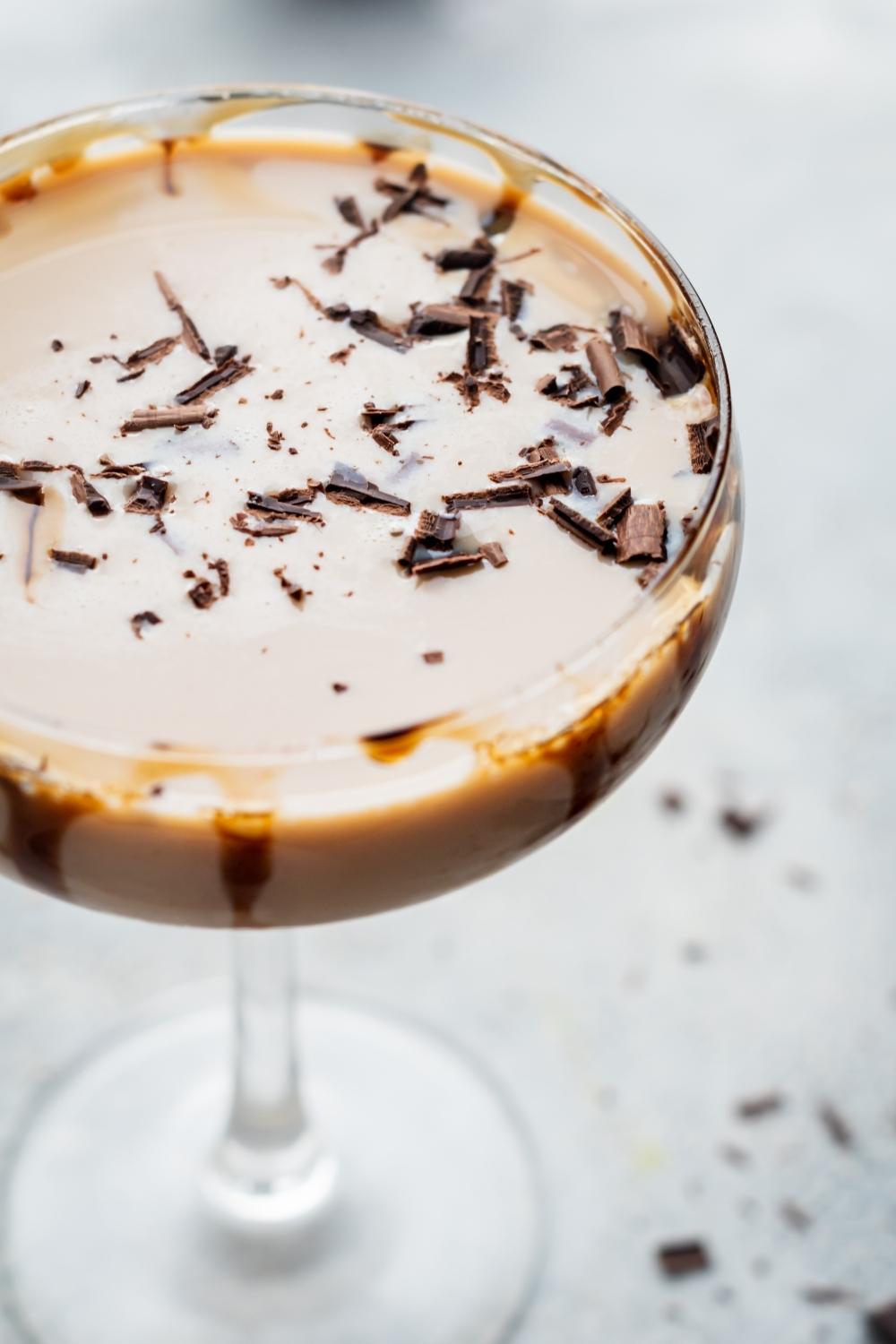 A close-up overhead view of a mudslide cocktail in a cocktail stemmed glass. It is garnished with shaved chocolate and there is drizzled chocolate on the inside of the glass.