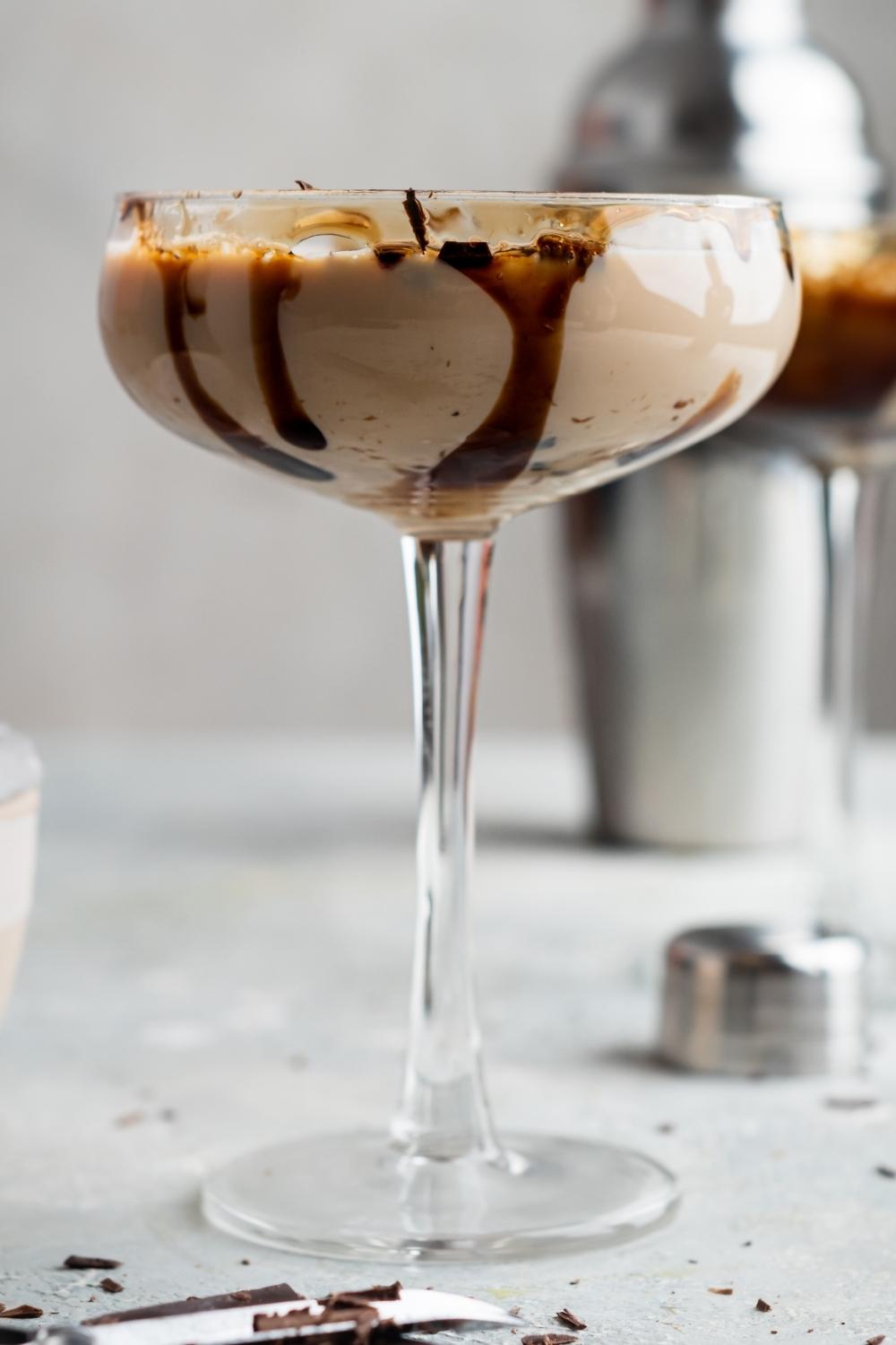 A profile view of a mudslide cocktail in a cocktail stemmed glass. It is garnished with shaved chocolate and there is drizzled chocolate on the inside of the glass.