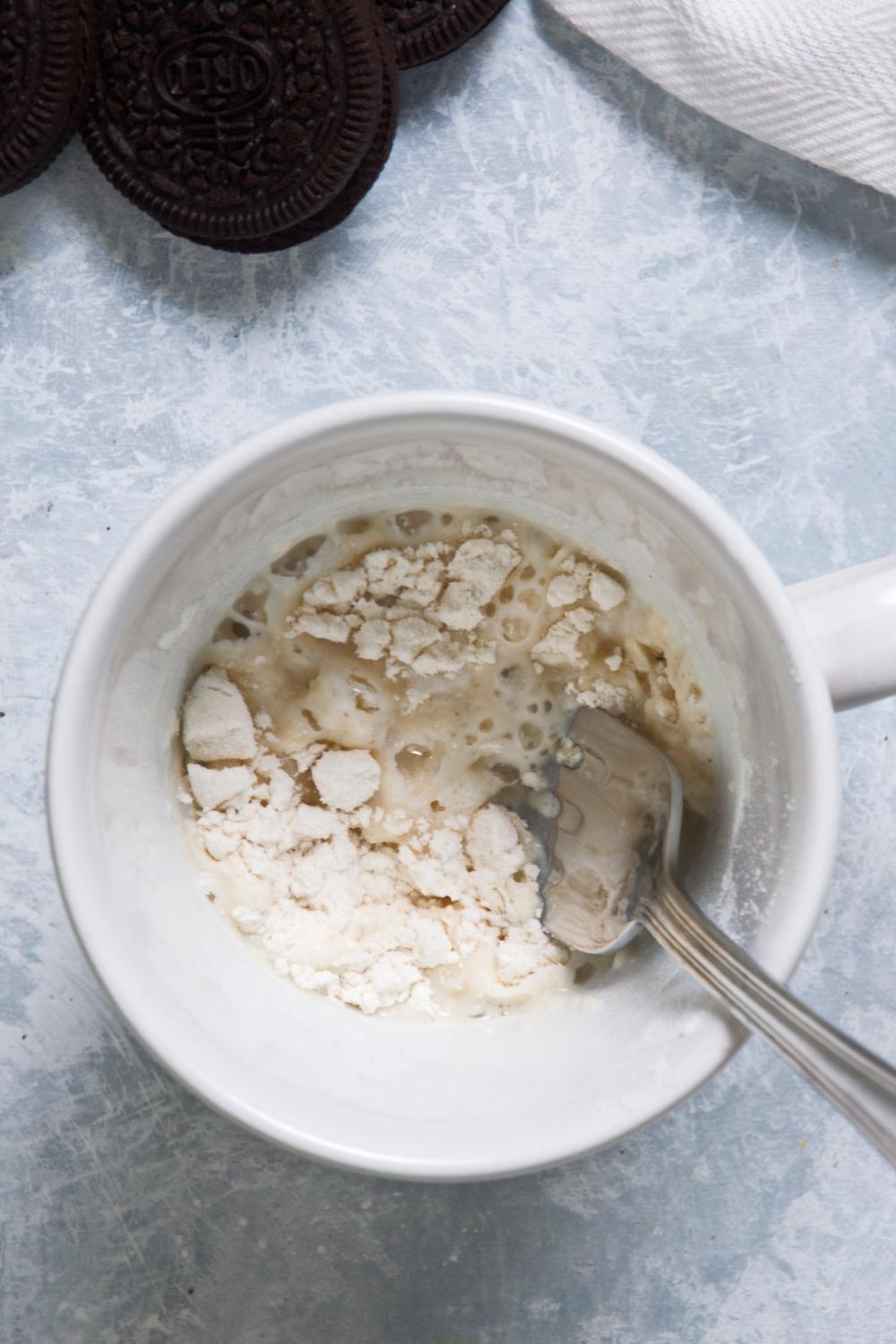 An overhead view of a mug containing flour and milk with a spoon in it.