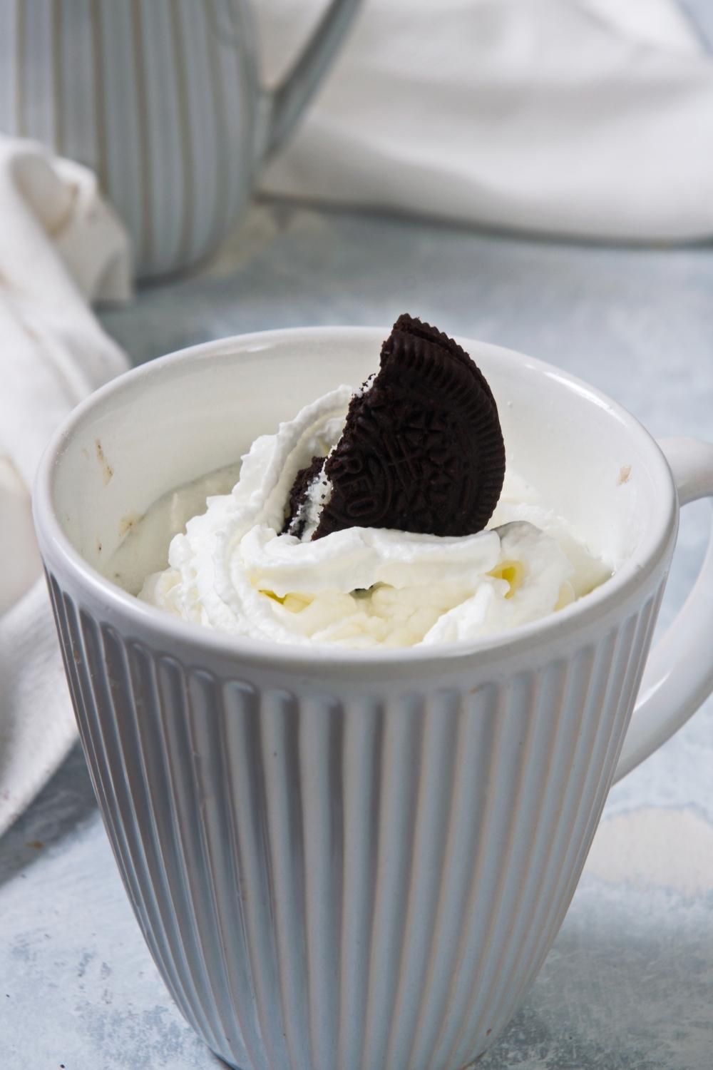 A close-up of a mug containing homemade Oreo mug cake topped with whipped cream and a half of an Oreo.