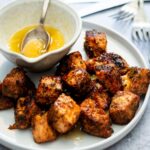A white plate with blackened salmon bites and a bowl with honey garlic sauce in it.