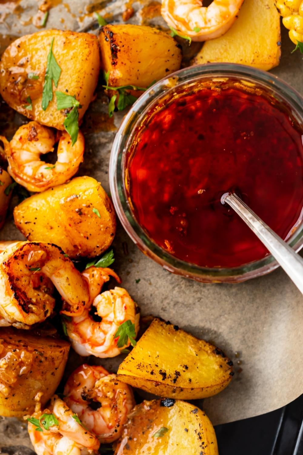 No review of a mason jar containing cooked seafood boil sauce. An arrangement of cooked veggies and shrimp surrounds it.