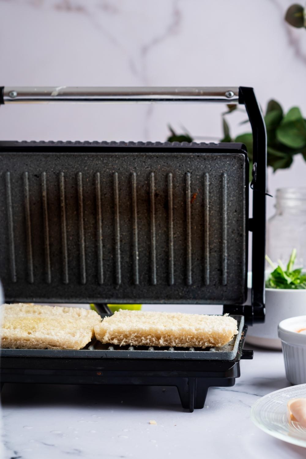 A Panini press with two focaccia halves on it.