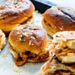 BBQ shredded chicken sliders on a parchment lined baking tray.