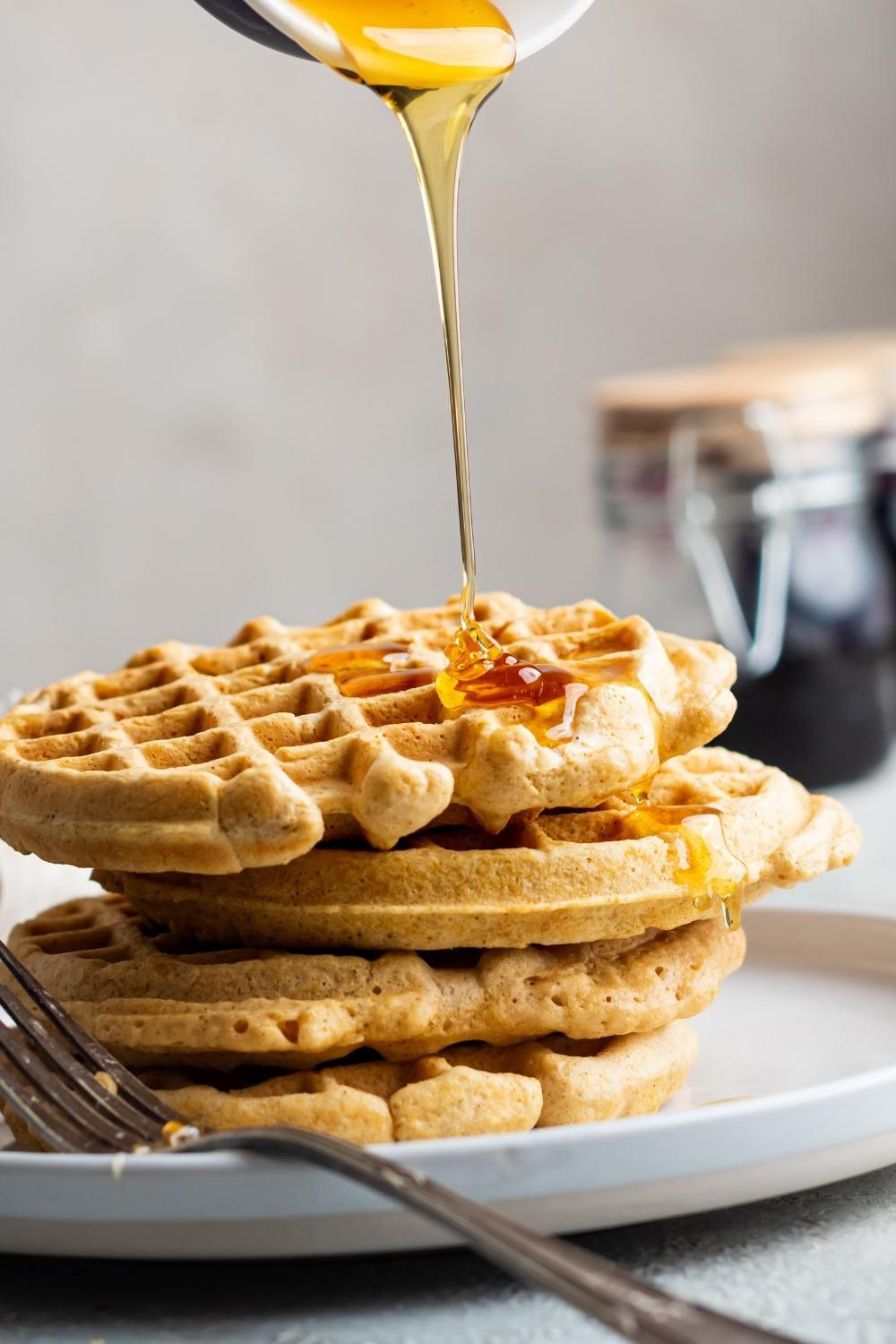 A stack of four homemade waffles without milk in drizzled with honey.