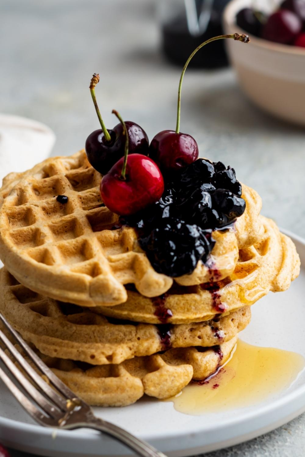 A stack of four homemade waffles without milk, drizzled with honey and topped with fresh berries and cherries.