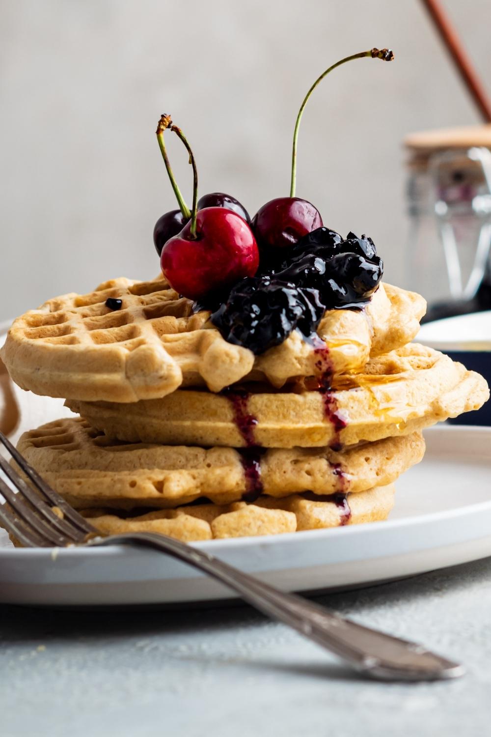 A stack of four homemade waffles without milk, drizzled with honey and topped with fresh berries and cherries.