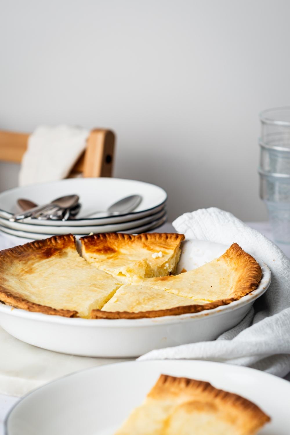 A ricotta pie in a pie dish with one slice missing from it.
