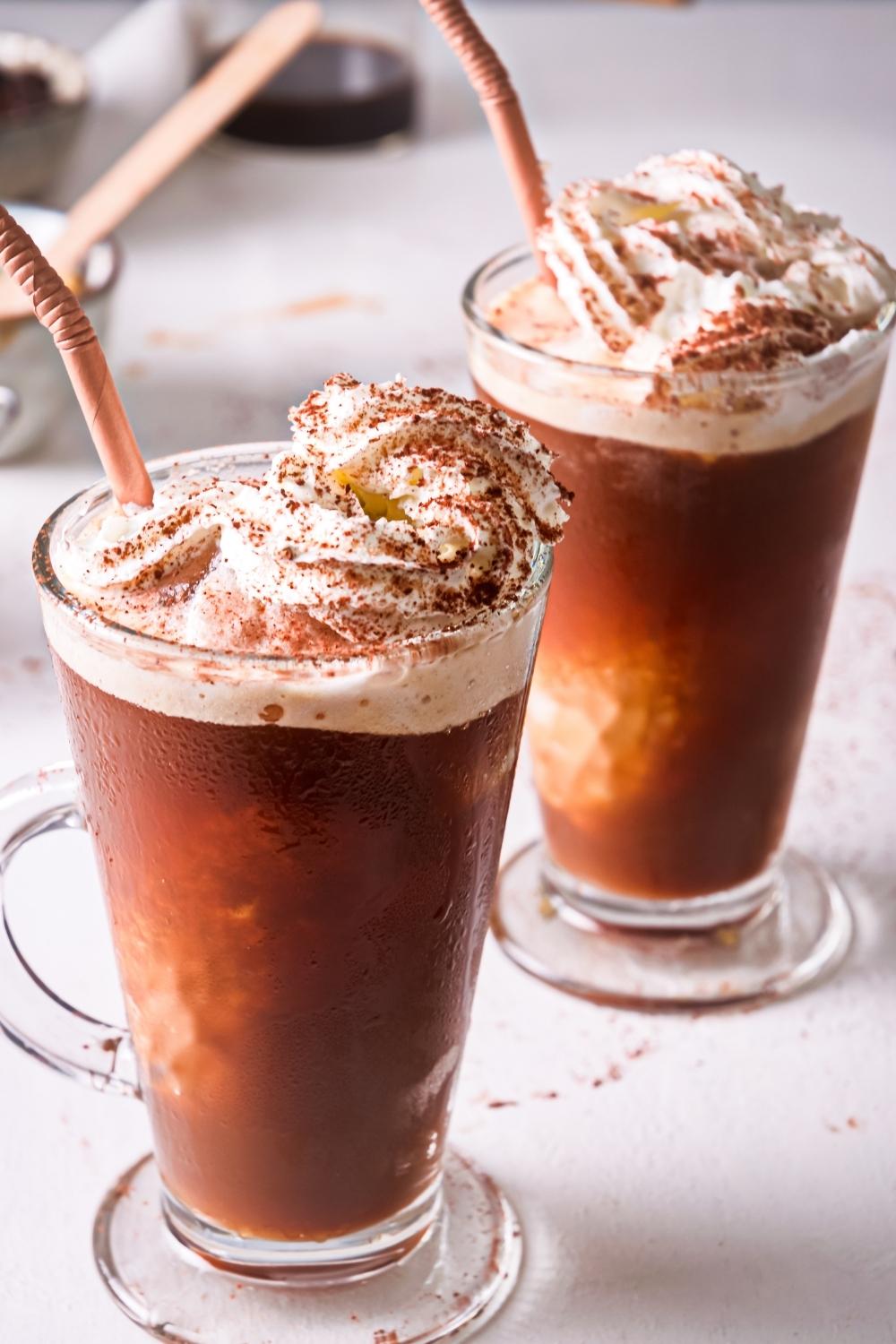 Two tall glasses of homemade McDonald's caramel frappe topped with whipped cream and sprinkled with cinnamon.