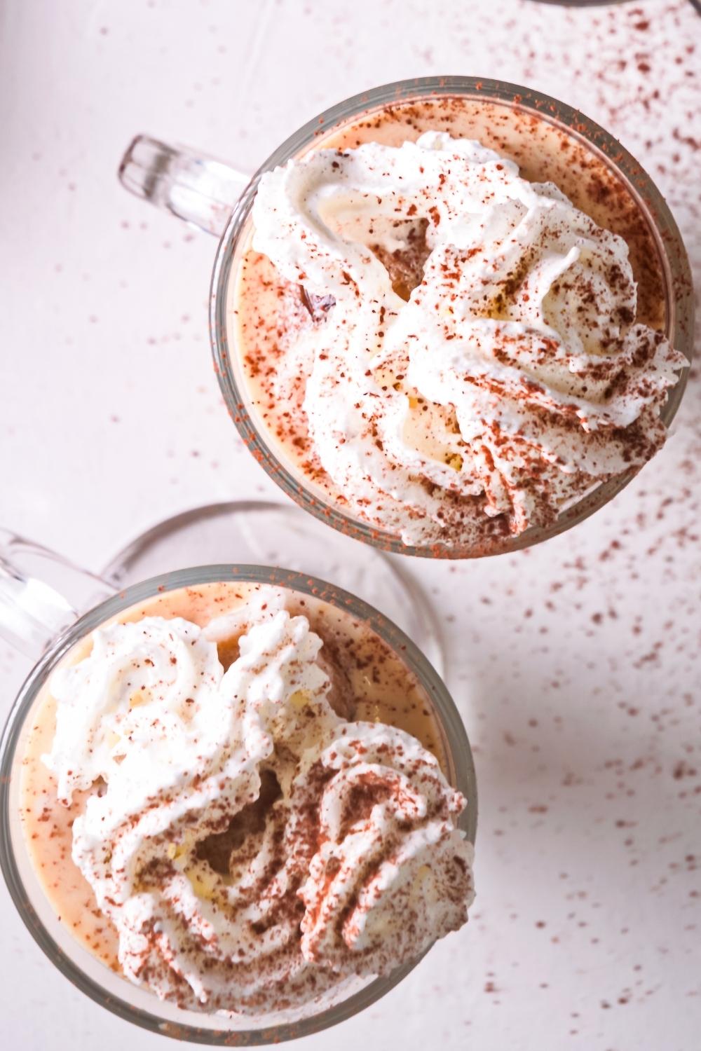 An overhead view of two tall glasses of homemade McDonald's caramel frappe topped with whipped cream and sprinkled with cinnamon.