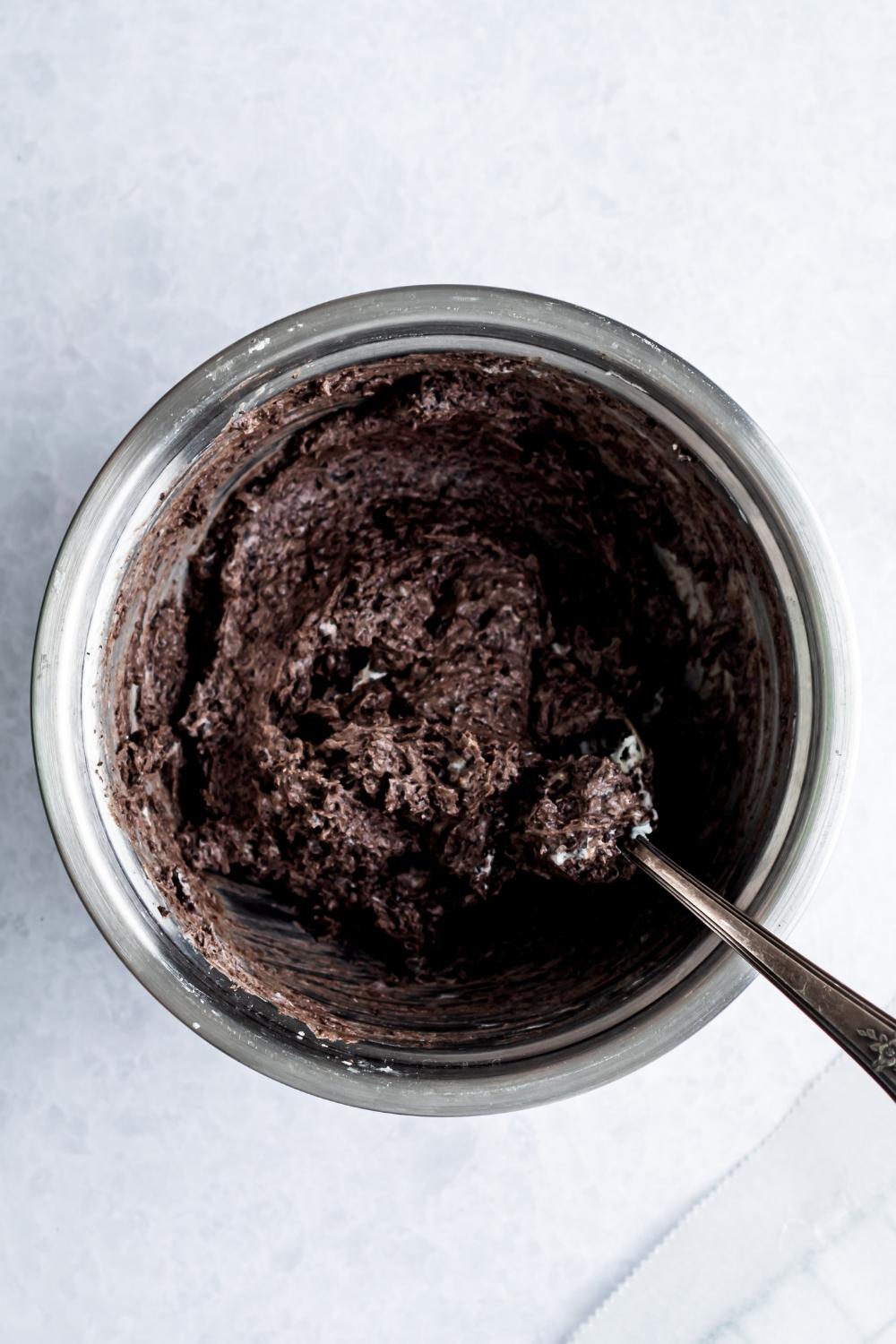 An overhead of a small bowl with crumbled oreos and cream cheese and a spoon is sitting in it.