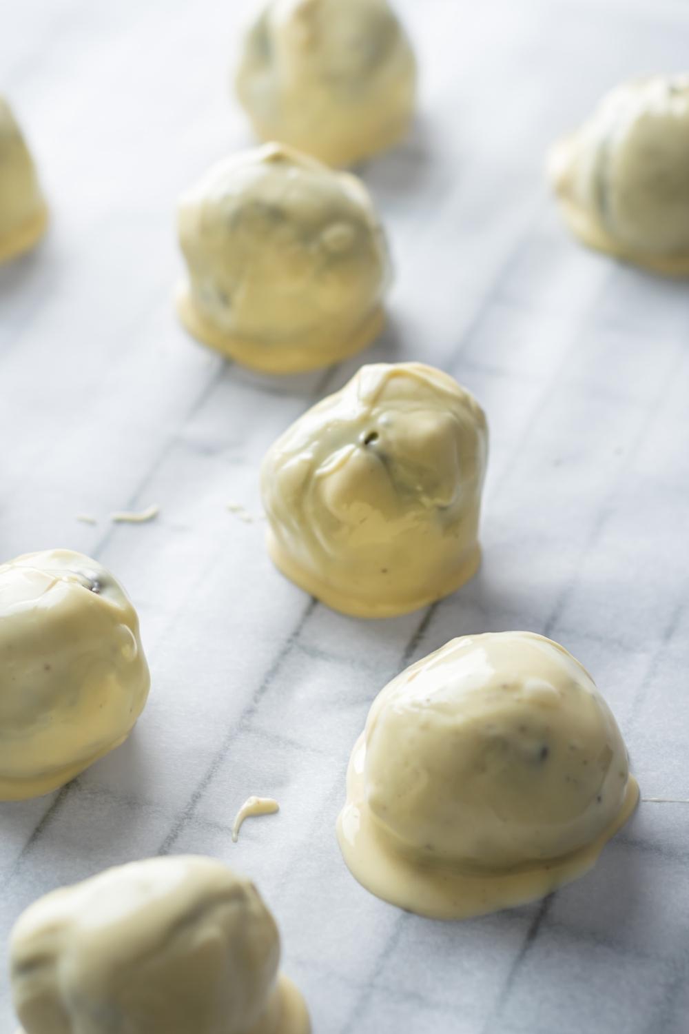 A close up of oreo balls on parchment paper lined wire rack, the oreo balls were freshly dipped in white chocolate.