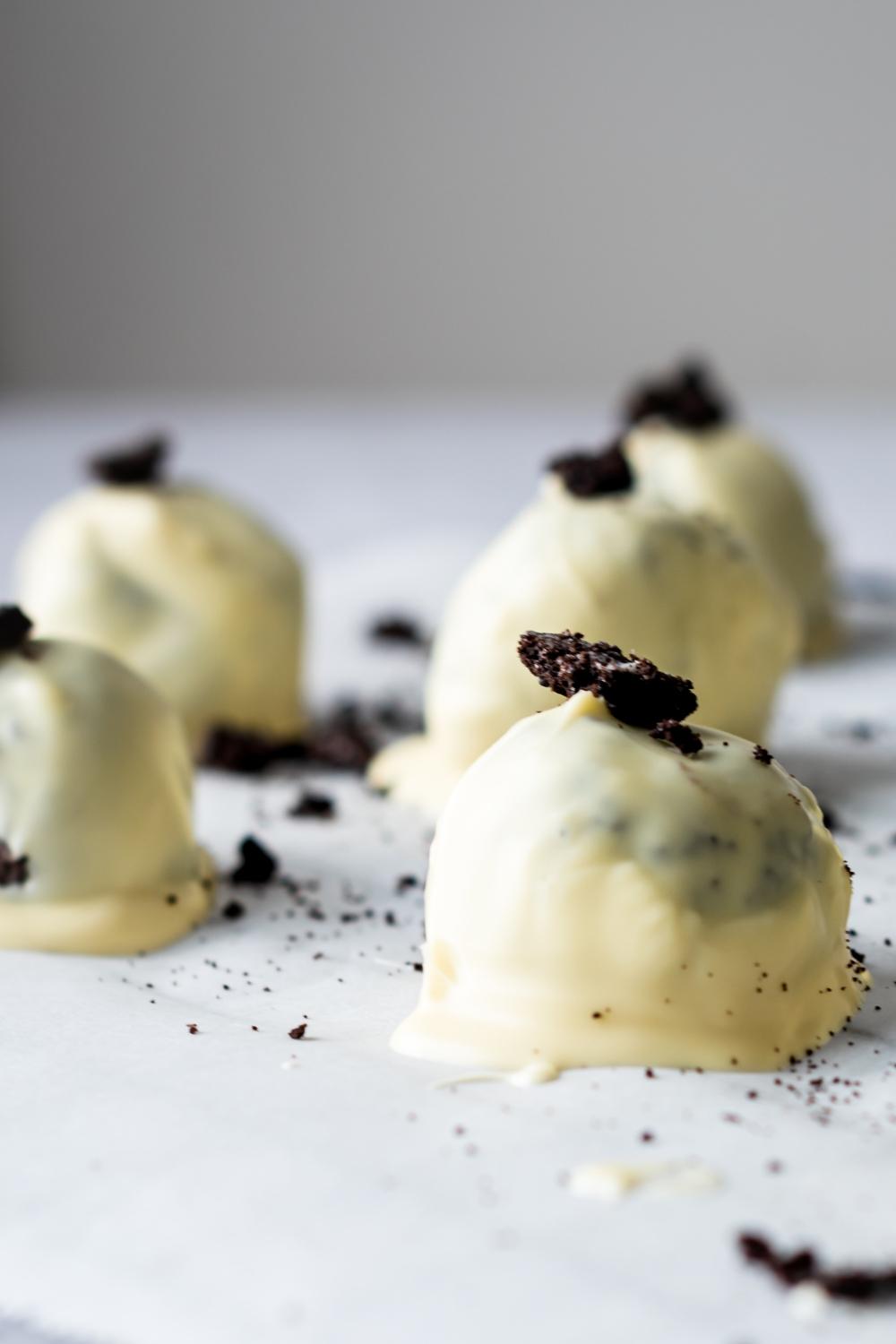 A close up of oreo balls on parchment paper. Each oreo ball is dipped in white chocolate and topped with crumbled oreos.