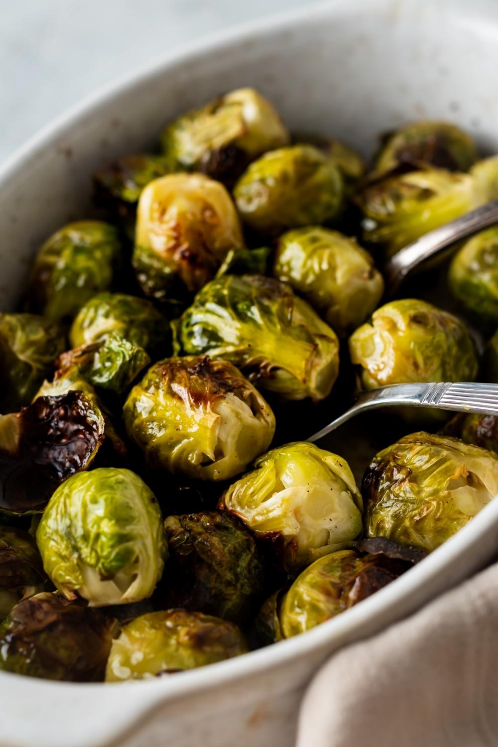 A casserole dish with cooked brussels sprouts. Two serving spoons sit in the dish.