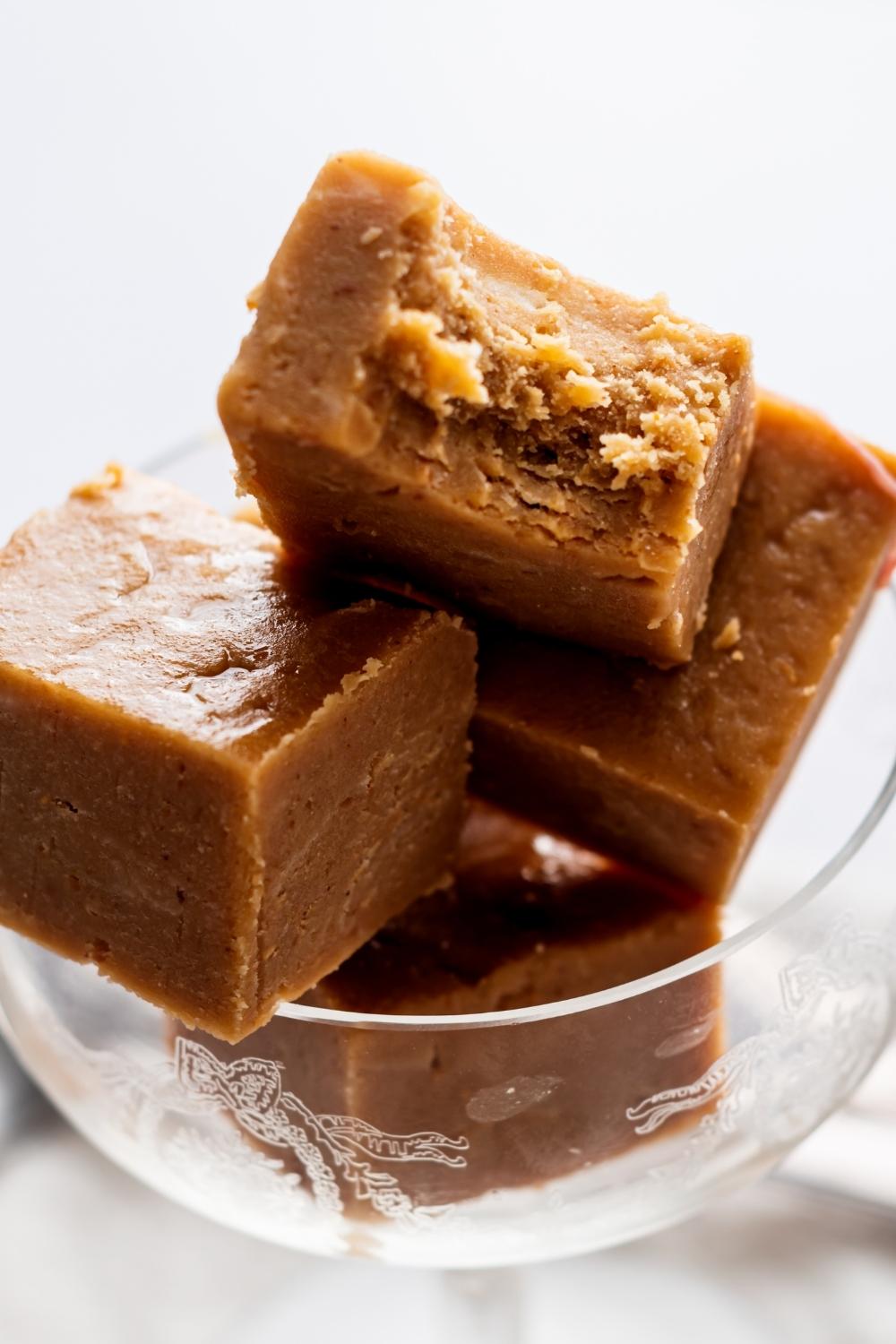 A close up of a cocktail glass with 4 squares of peanut butter fudge in it. The top square has a bite taken out of it.