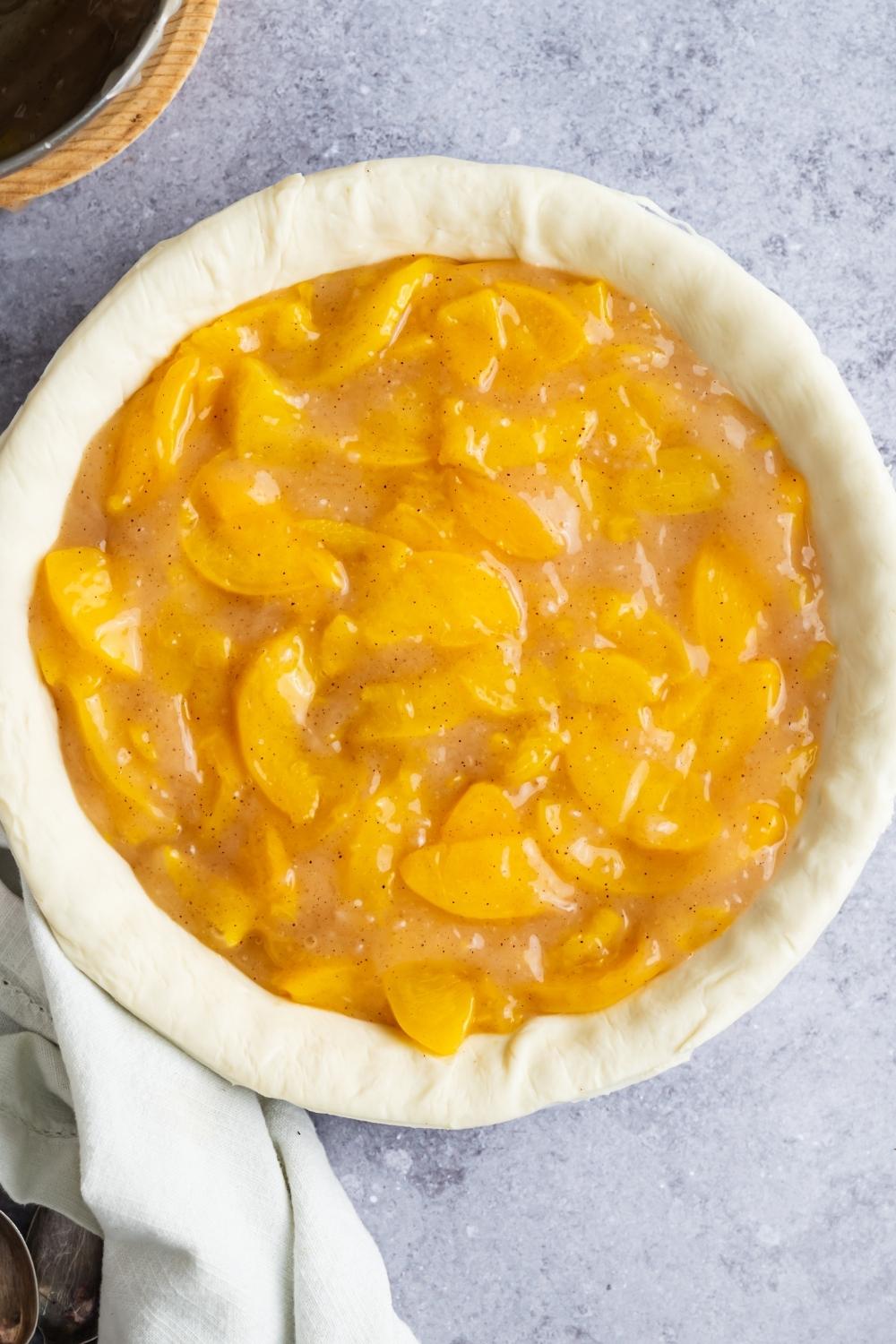 An overhead view of a pie dish with pie crust dough and peach pie filling on top of it.