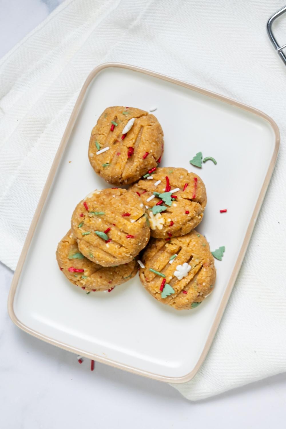 Red, white, and green sprinkles on top of five no bake peanut butter cookies on a white plate.