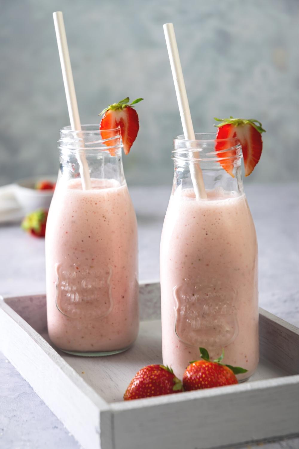 Two strawberry banana smoothies in glasses with a straw in it and sliced strawberry on the rim.