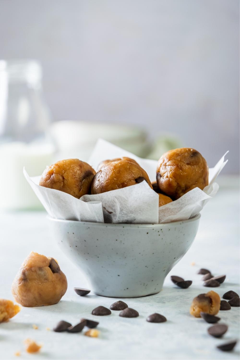 A bunch of edible cookie dough bites on top of parchment paper in a bowl.