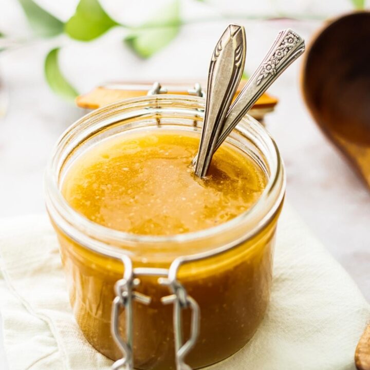 A glass jar that is filled with brown gravy with two utensils.