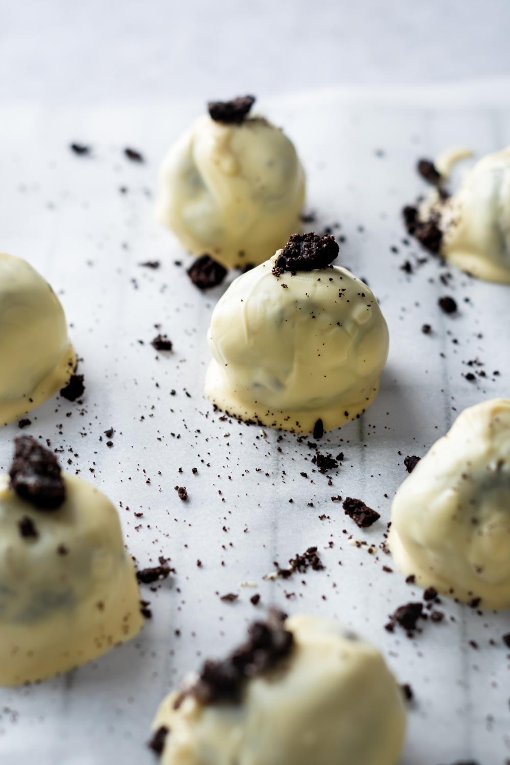 A close up of oreo balls on parchment paper. Each oreo ball is dipped in white chocolate and topped with crumbled oreos.