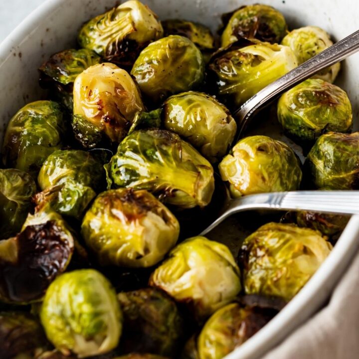 A casserole dish with cooked brussels sprouts. Two serving spoons are siting in it.