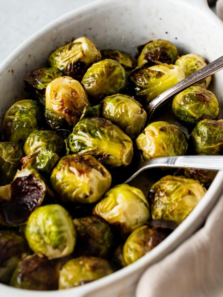 A casserole dish with cooked brussels sprouts. Two serving spoons are siting in it.