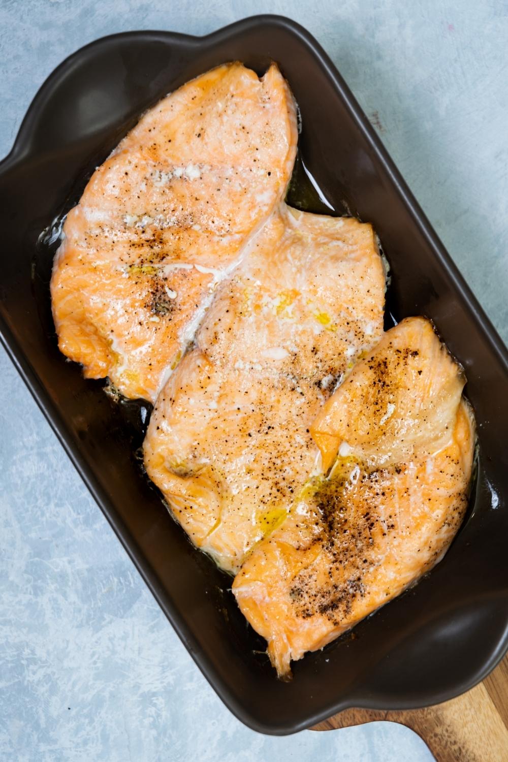 Three baked salmon fillets in a rectangular dish.